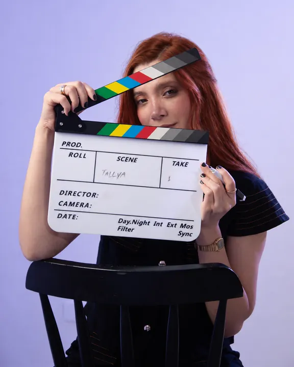 Amanda Tallya com uma claquete em fundo lilás